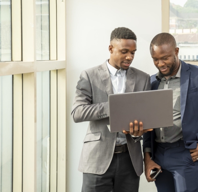 Two young black businessmen standing together holding a laptop, discussing business