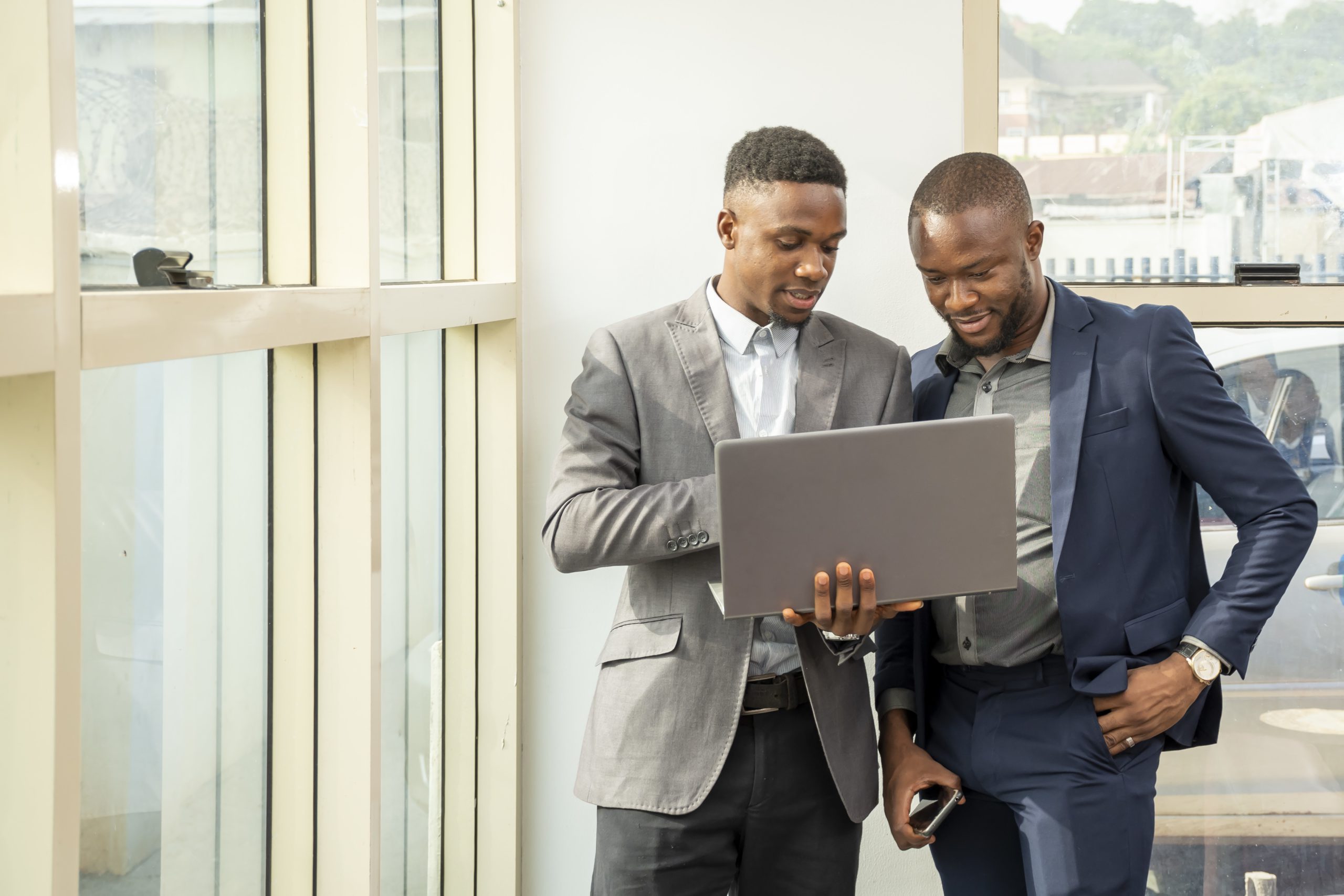 Two young black businessmen standing together holding a laptop, discussing business